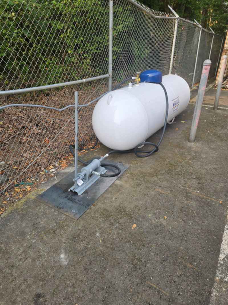 A residential propane tank in a fenced yard with the gauge dome closed.